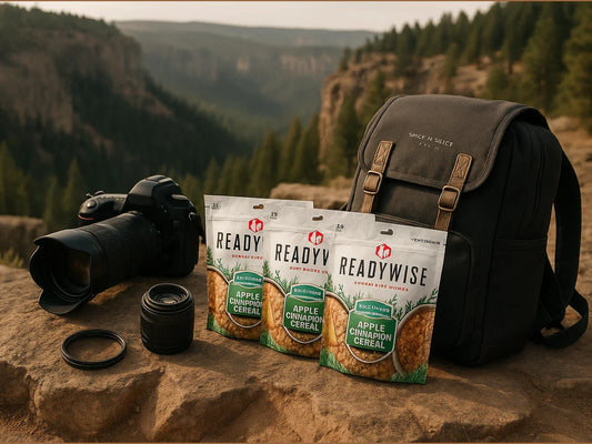 ReadyWise Apple Cinnamon Cereal pouches with camera gear and backpack on rocky cliff outdoors