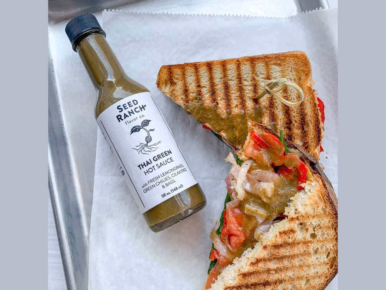 Classic Heat Trio - 3 Bottle Bundle with Thai Green hot sauce and sandwich on tray.