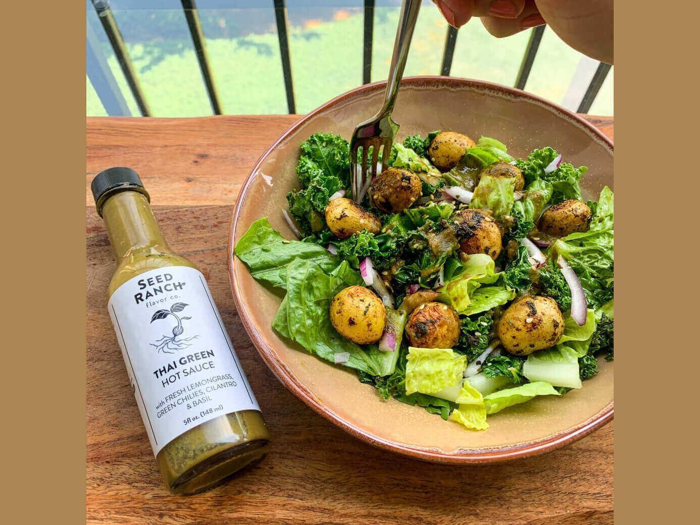 Fresh Thai salad with baby potatoes, mixed greens, and Thai green hot sauce bottle