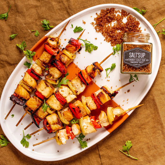 Grilled chicken and vegetable skewers on a white plate with coarse smoked salt and parsley garnish