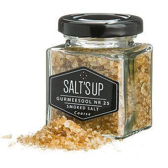 Square glass jar of Salt's Up smoked coarse salt with some salt spilled beside it