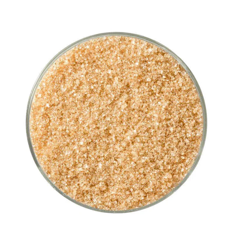Close-up of light brown raw sugar crystals in a round glass container on white background