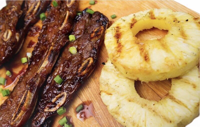 Grilled marinated beef short ribs with green onions and pineapple rings on wooden board