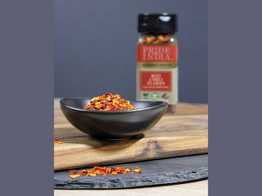 Red chili flakes in a black bowl with Pride of India red chili flakes jar in background