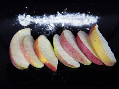 Sliced apple wedges with red peel and a line of white powder on a glossy black surface