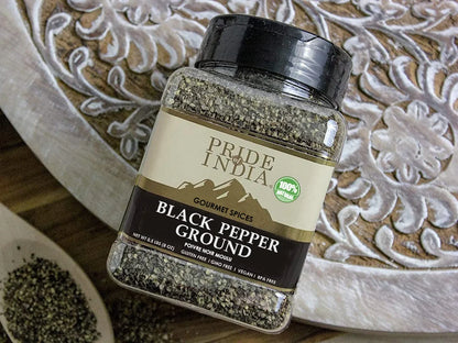 Pride of India ground black pepper bottle on a decorative wooden surface with peppercorns