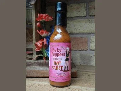 Perky Peppers chipotle hot sauce bottle on wooden table with flowers and brick background
