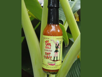 Cin Chili Serrano hot sauce bottle on green tropical plant, spicy condiment label visible