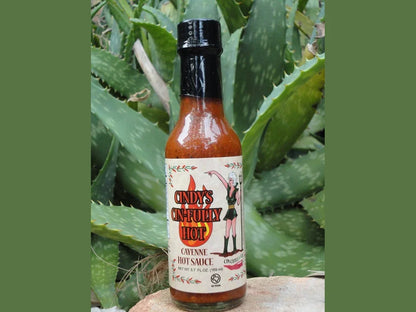 Cindy's Sinfully Hot cayenne hot sauce bottle with aloe vera plants background