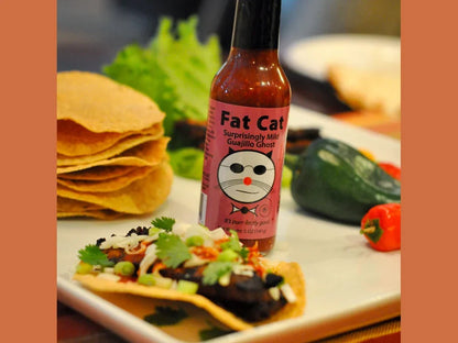 Fat Cat Guajillo Ghost hot sauce bottle on plate with tostada, peppers, and tortillas