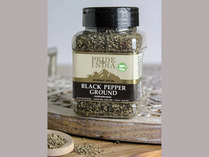 Ground black pepper in glass jar with wooden spoon on rustic kitchen table

