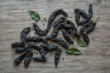 Dried black chilies and green leaves on rustic wooden background