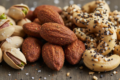 Close-up of spicy roasted almonds, salted pistachios, and seasoned cashews on wooden surface