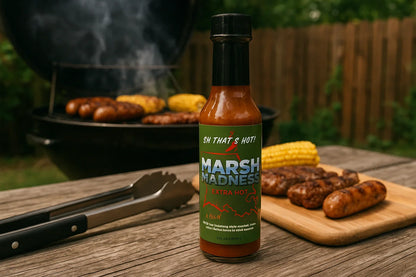 Marsh Madness extra hot sauce bottle on picnic table with grilled sausages and corn at barbecue