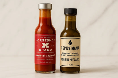 Two bottles of hot sauce on a white surface: Horseshoe Brand Korean Ginger and 1 Spicy Mama Original